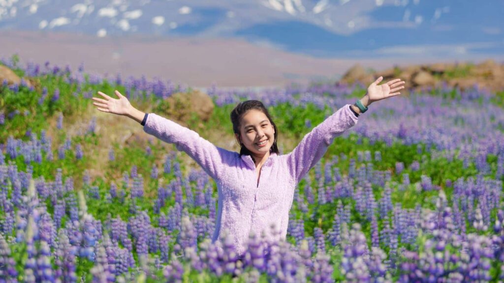 Attractive happy asian woman standing and smiling in a lupine flower field on Iceland