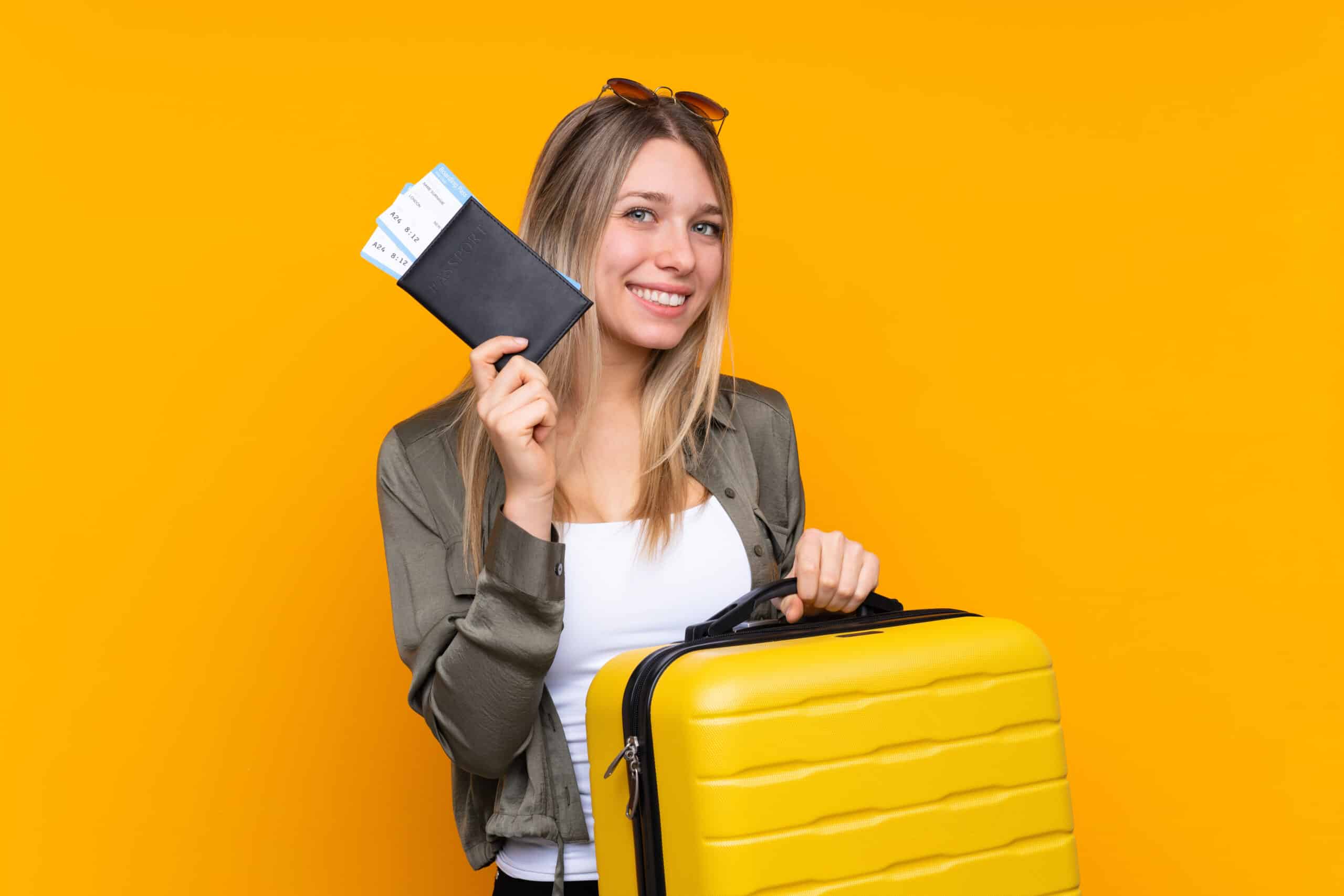 Young blonde woman over isolated yellow background in vacation with suitcase and passport