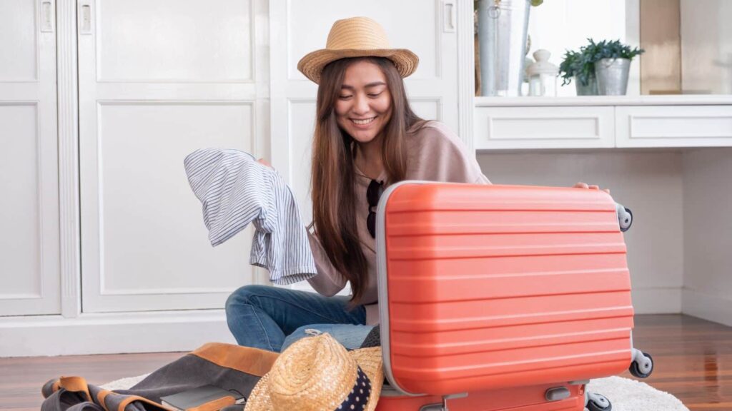 Young Asian traveler preparing for a trip packing a red suitcase