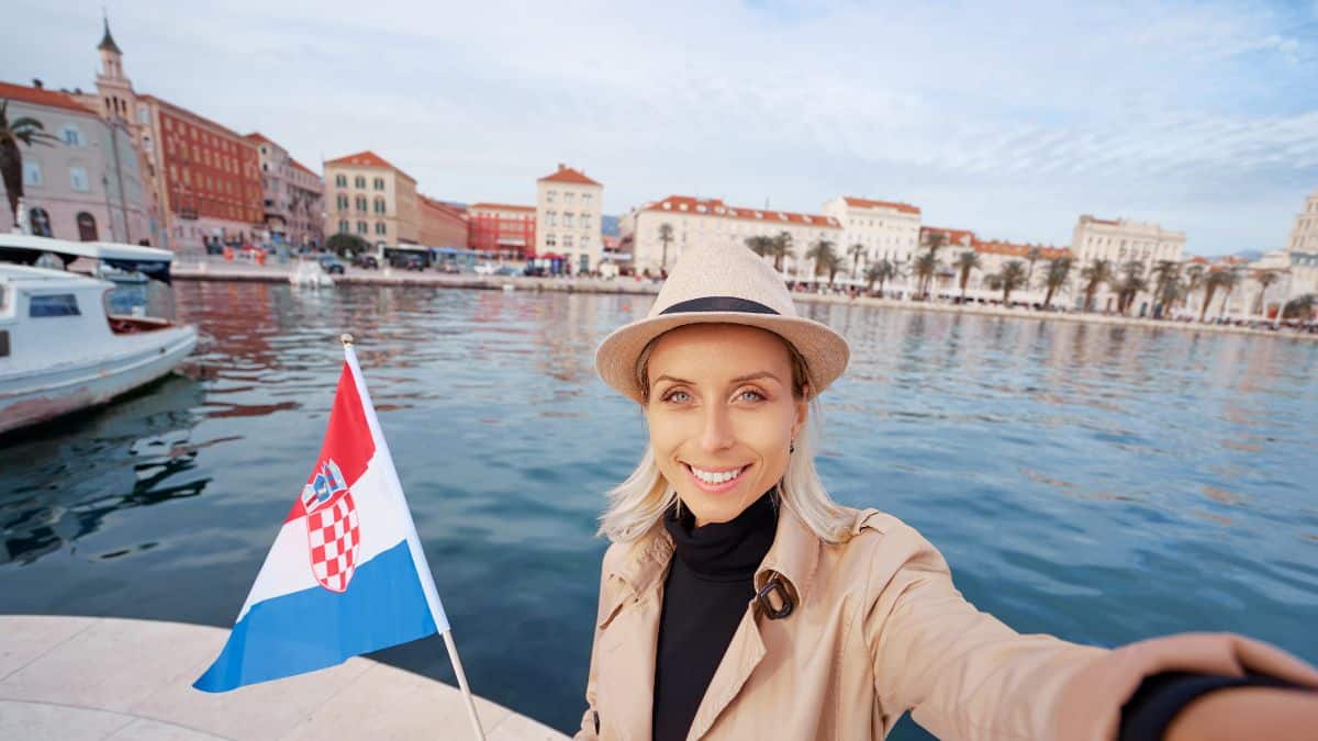 Enjoying vacation in split Croatia. Travel and technology. Young woman with national croatian flag taking selfie on Split sea shore promenade.