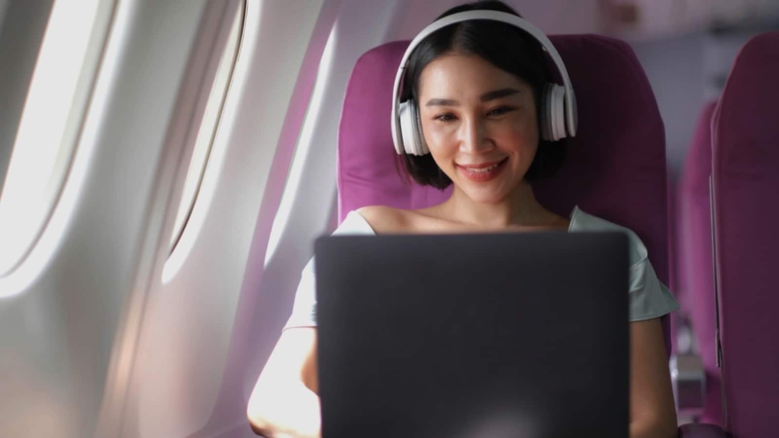 Woman in flight using laptop with noise cancelling headphone