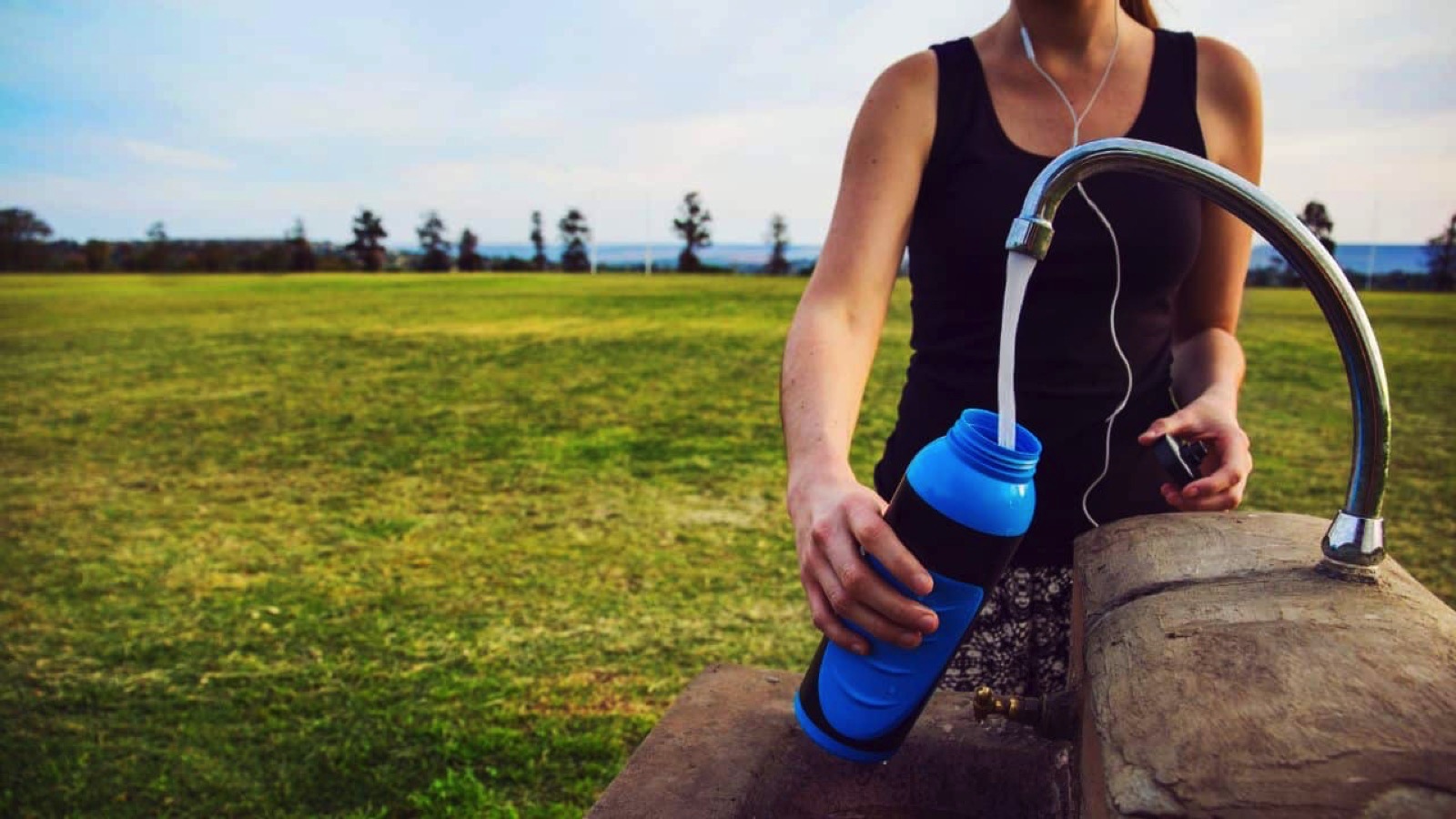 Female runner fills up water bottle outdoors at the public park