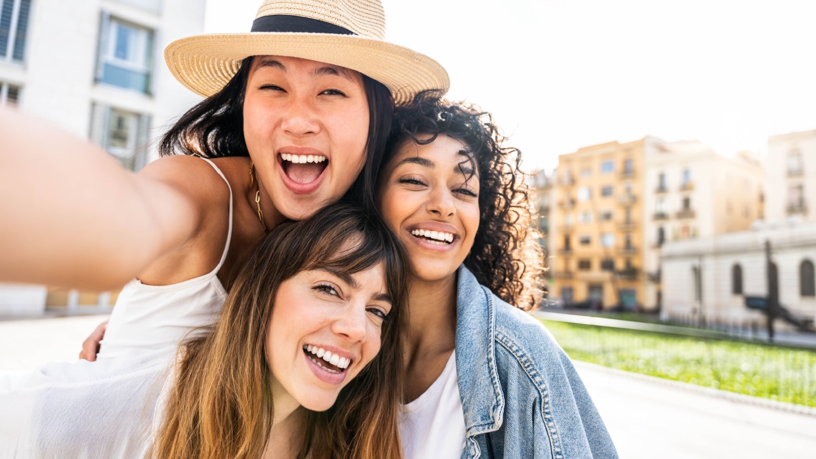 Multiracial three young women taking selfie portrait on city street; happy female friends having fun together hanging outside