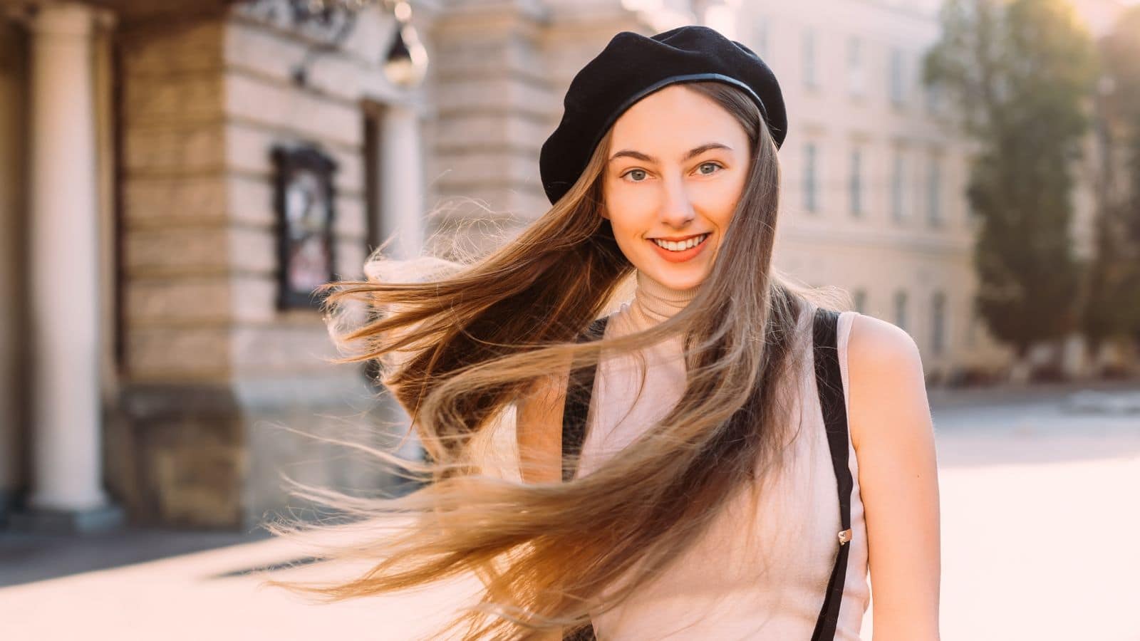 beautiful girl in a stylish black beret smiling in the camera lens and the wind disperses the hair