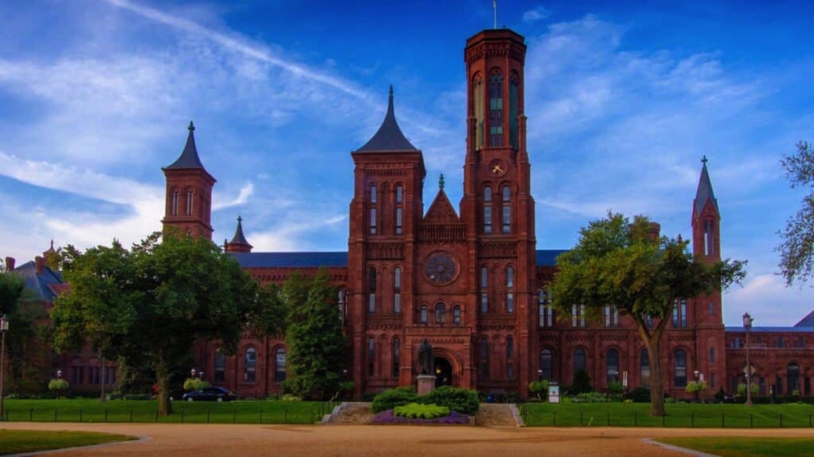 front entrance view of the red brick Smithsonian Institute Castle on the national mall with ornate gardens and statues in front.