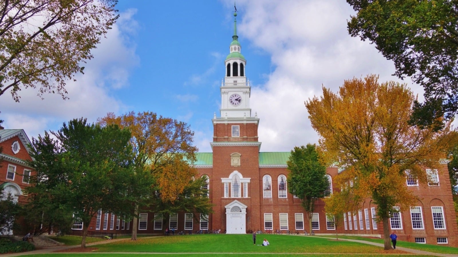 Looking down the Dartmouth Green with trees beginning to show fall colors and a blue sky with puffy white clouds on a nice autumn day the Baker Library and its bell tower is in the background.