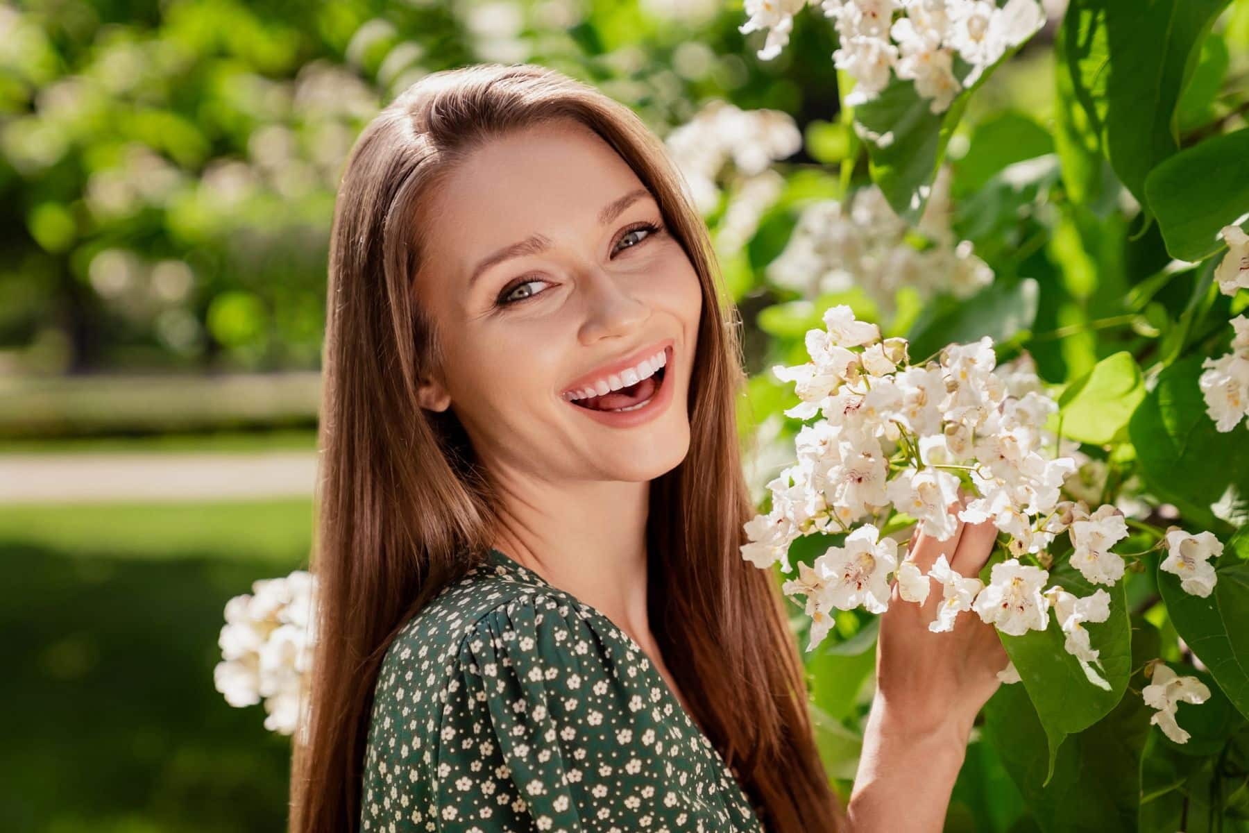 Photo-of-positive-brunette-happy-cheerful-woman-smile-spring-flowers-trees-enjoy-outdoors-outside-park-street