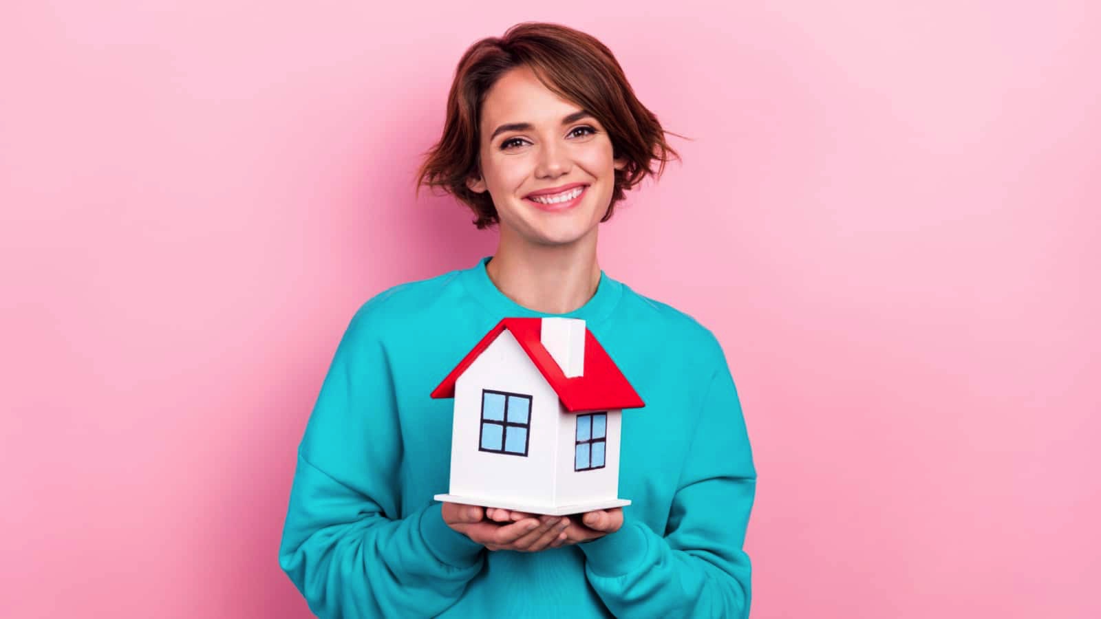 Pretty-cheerful-girl-in-a-stylish-pullover-holding-miniature-house