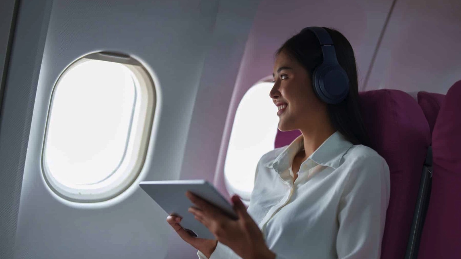 Young-Asian-attractive-business-woman-passenger-sitting-on-business-class-luxury-plane-while-wearing-wireless-headphone