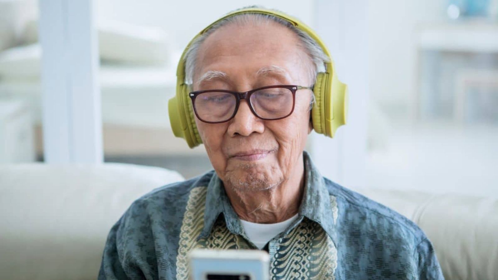 Close up of old man enjoying music with a mobile phone and headphones in the living room at home