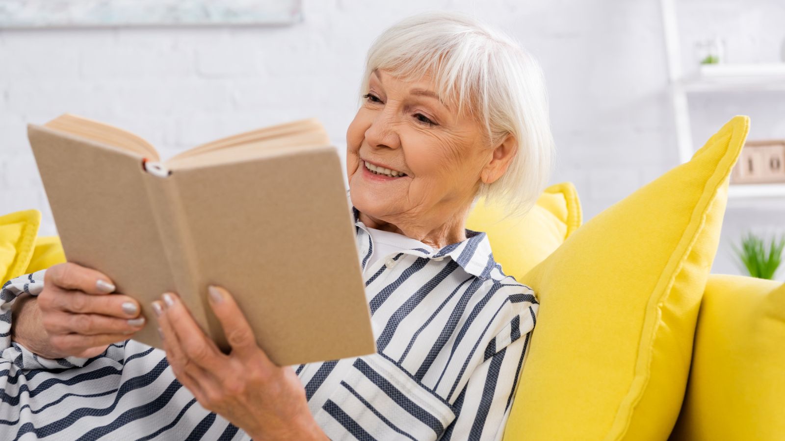 senior woman reading a book on a yellow couch